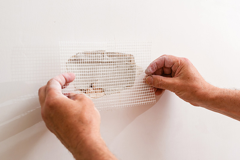home-drywall-repair Hands applying mesh patch over hole in drywall during wall repair process.