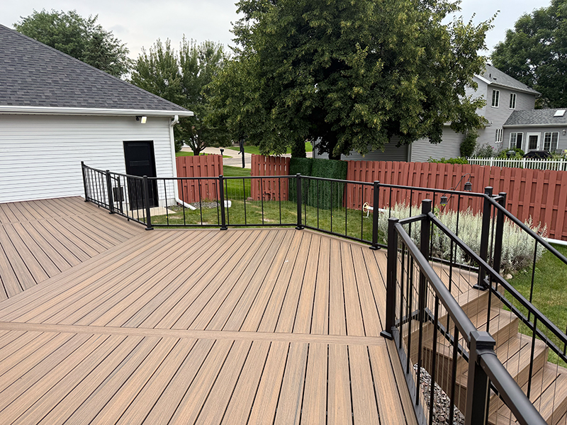 kvl-construction-gallery-08 Spacious composite deck with modern black metal railing and steps leading to the backyard, framed by a red privacy fence and lush landscaping.