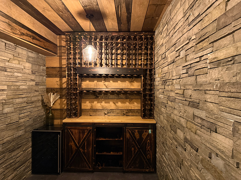 kvl-construction-gallery-25 Rustic home wine cellar with stone walls, wood ceiling, custom wine racks, and bar counter with storage cabinets.